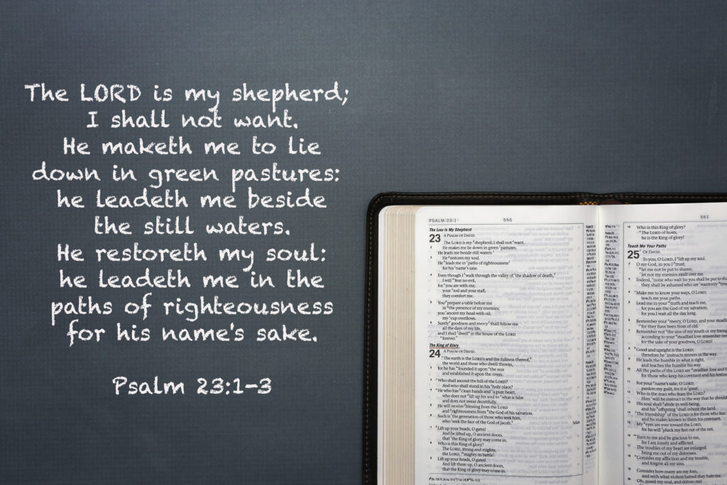 An open Bible next to a chalkboard with Psalm 23:1-3 written in chalk, an example of the characteristics of the righteous. 