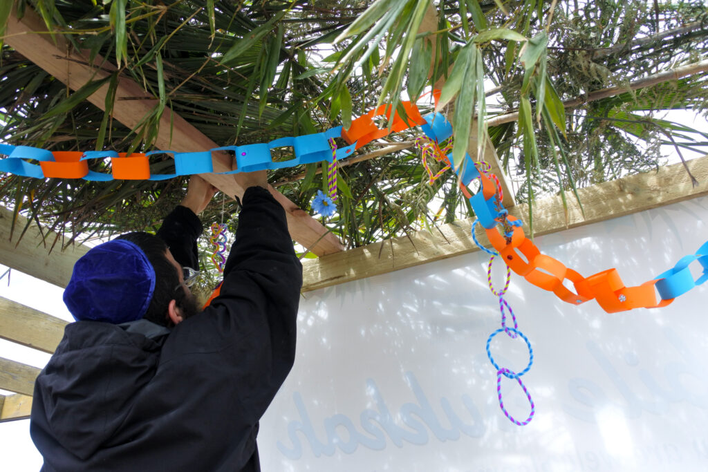 Jewish man putting up decorations during sukkot. By doing this he is teaching your children about sukkot.