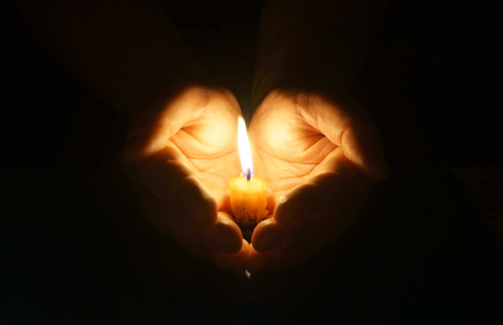 A pair of hands holding a candle using its flame to position yourself for protection.