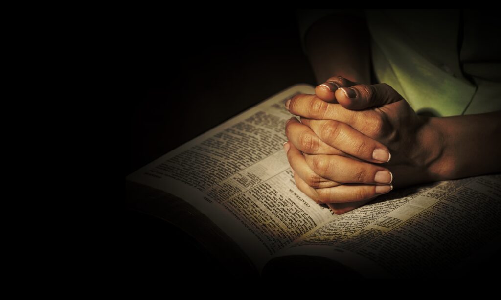 A person alone in the dark, praying over their Bible.