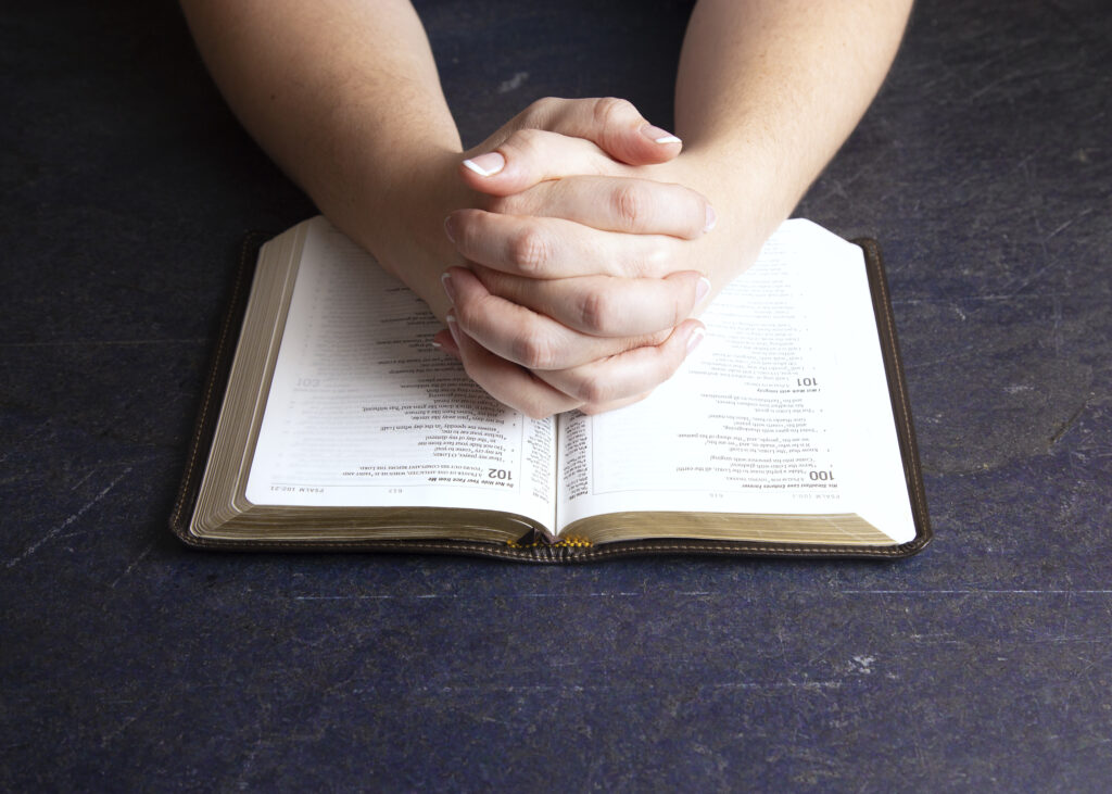 Woman's hands praying over the Bible trying to identify the generational curses.