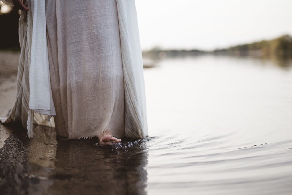 Closeup shot of a person wearing a biblical robe walking in the water near the shore as Jesus. 