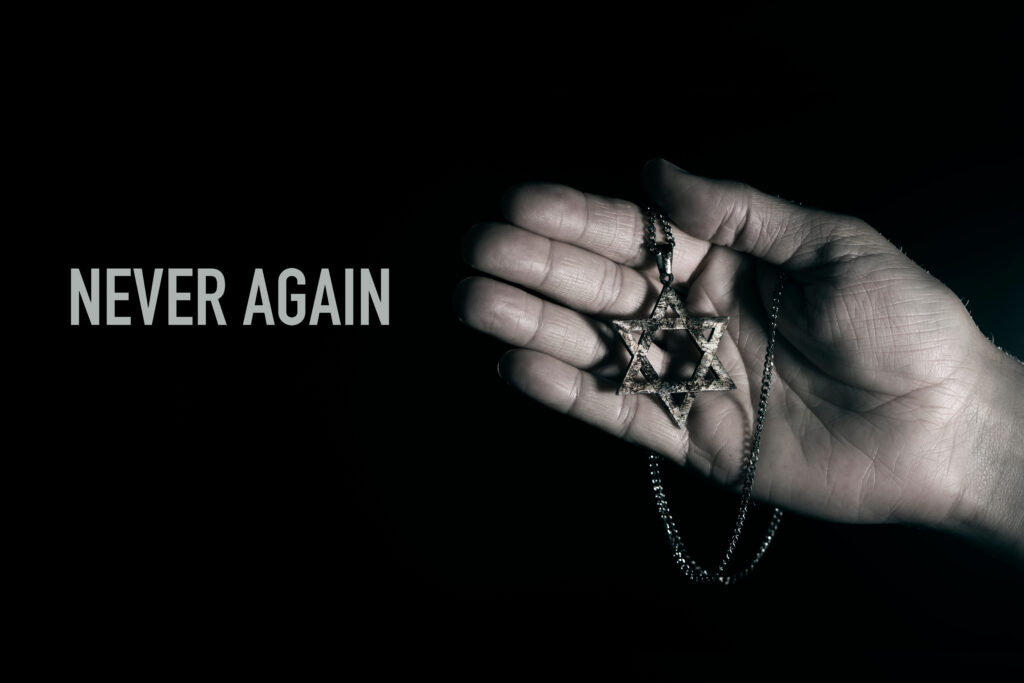An open hand holds a necklace with the star of David with the words “Never Again”