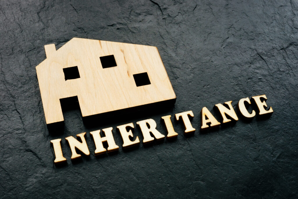 A wood block house and letters that say "inheritance" on a black stone.