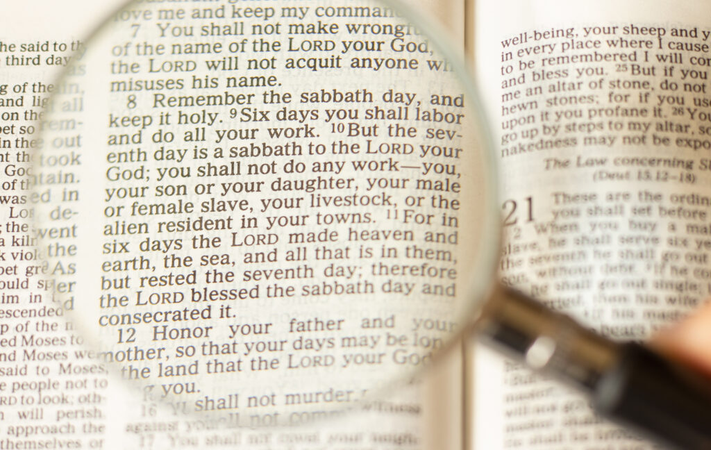 A magnifying glass raised up to a Bible to highlight the fourth commandment.