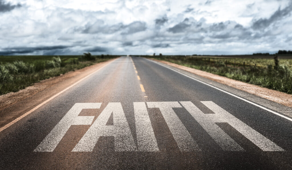 A long road in the middle of nowhere with the word "faith" painted across it.