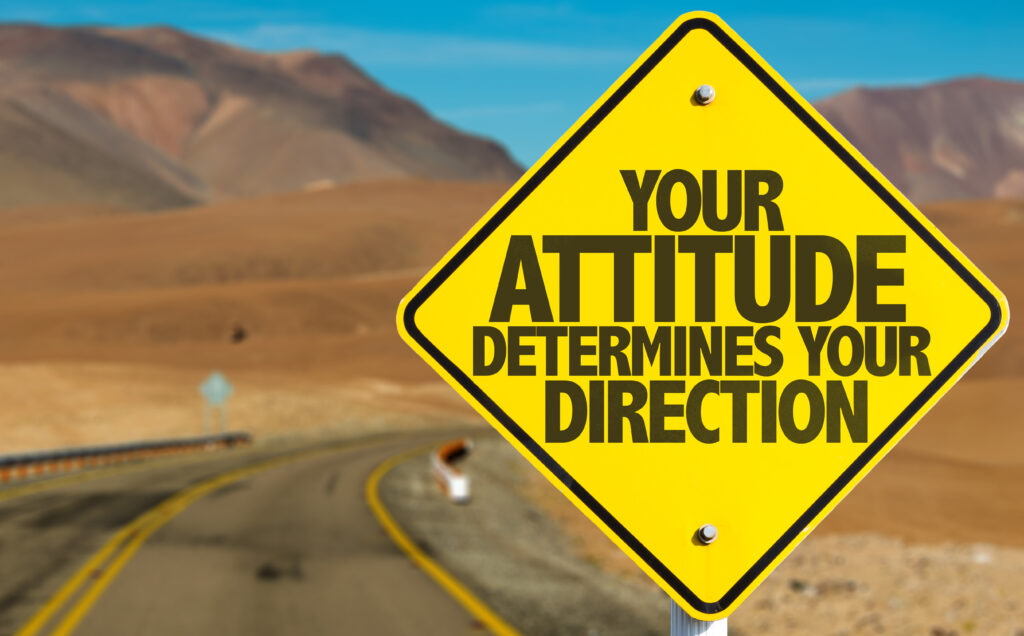 Yellow road sign on a desert highway that reads your attitude determines your direction and that we need to adjust our attitude to be on the right path.