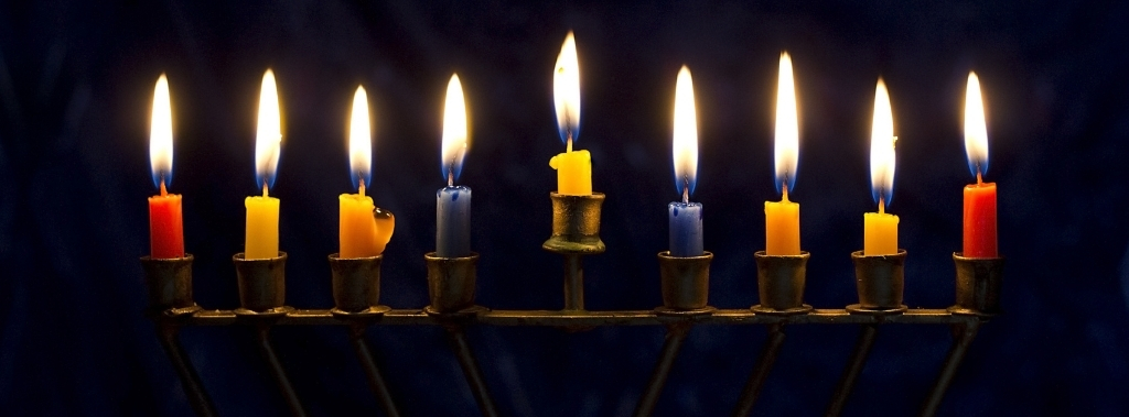 A hanukkiah with blue, red, yellow, and orange candles on a dark blue background.