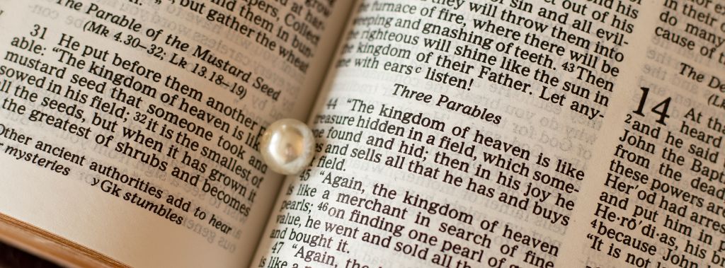 A pearl resting in the middle of an open Bible open to the Three Parables.