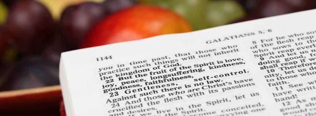 Close-up of Bible open to Galatians 5:22 about fruit of the spirit with fruit in the background.