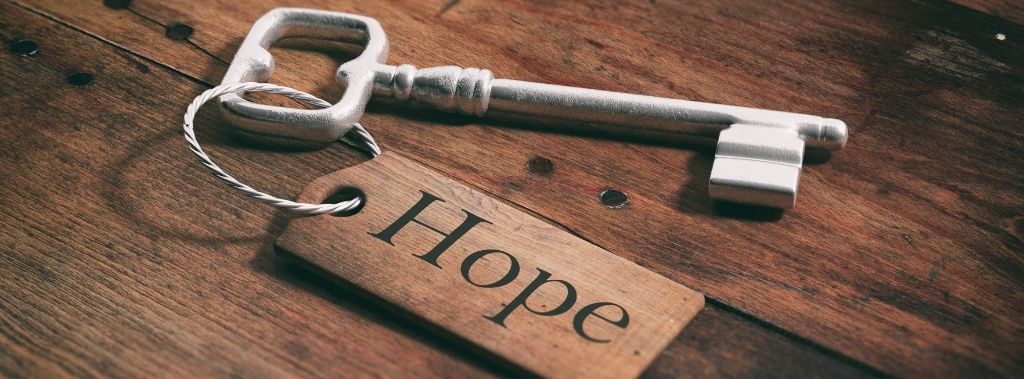Old silver key with a wooden tag with the word hope resting on a wooden background.
