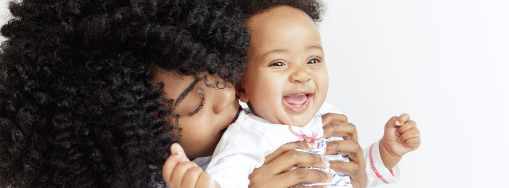 Young mother holding her smiling happy baby in front of white background.