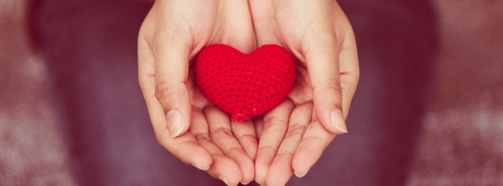 Woman holding a red yarn heart in the palm of her hands.