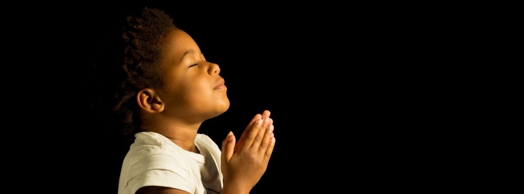 A young girl with eyes closed praying to represent faith in God.