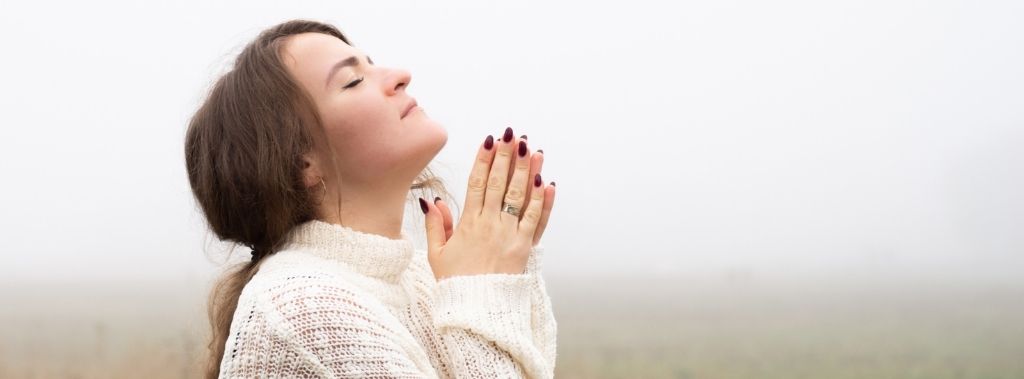 Brunette girl closing her eyes and praying in a fog-filled field as a warrior of God.