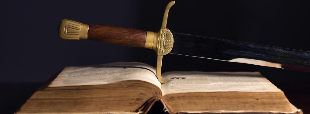 Wood and gold hilted sword on top of open Bible.
