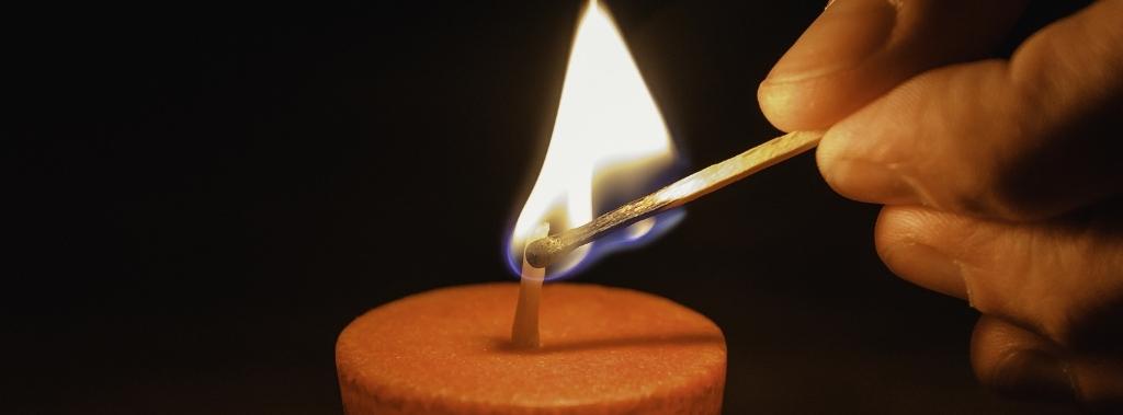 A close up of a hand lighting a candle with a match on a dark background.