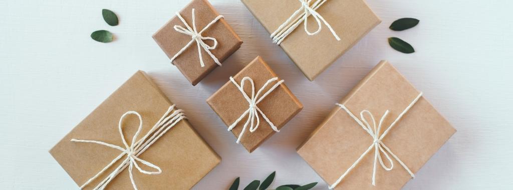 Craft gift boxes on white wooden background with green leaves scattered.