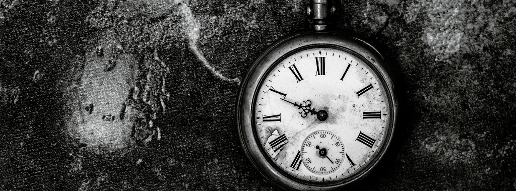 Black and white photo of broken pocket watch lying on the ground.