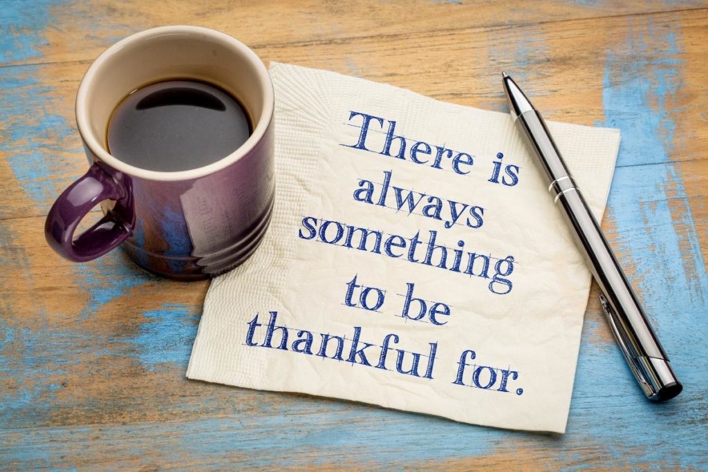 A napkin that says "There is always something to be thankful for." next to a pen and cup of coffee on a wooden background.