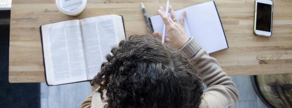 Overhead view of woman reading the Bible and writing in a notebook.