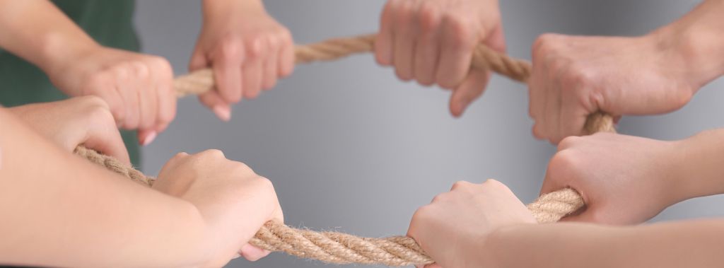 Close-up of four sets of hands holding on to a looped rope.