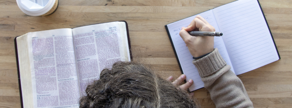 A woman sitting at a table looking at a Bible and journaling.