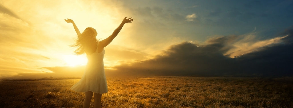 Woman in a white dress rejoicing in a field during sunrise.
