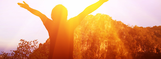 A person with their hands up in the air, celebrating as the sun shines on them.
