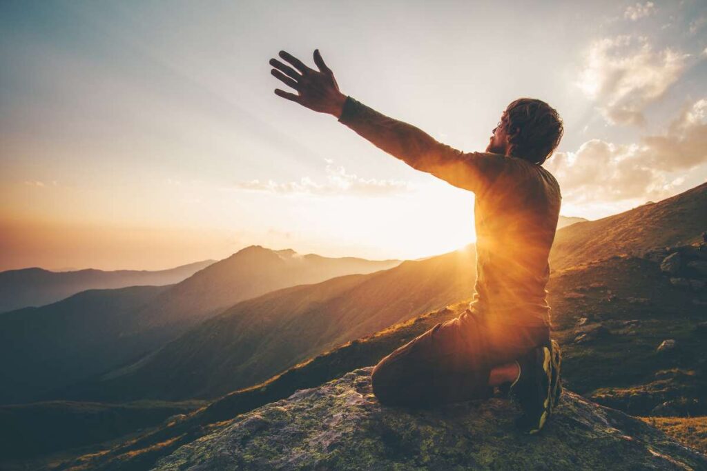 Man praying for Godly wisdom at sunset on mountain, arms raised in intercessory prayer.